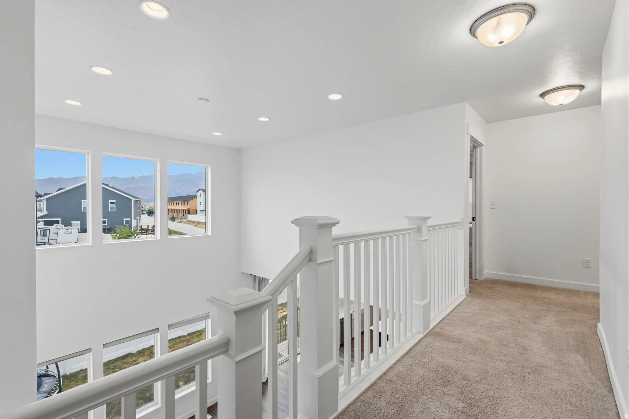 Upper-level landing featuring a white railing and neutral carpeting