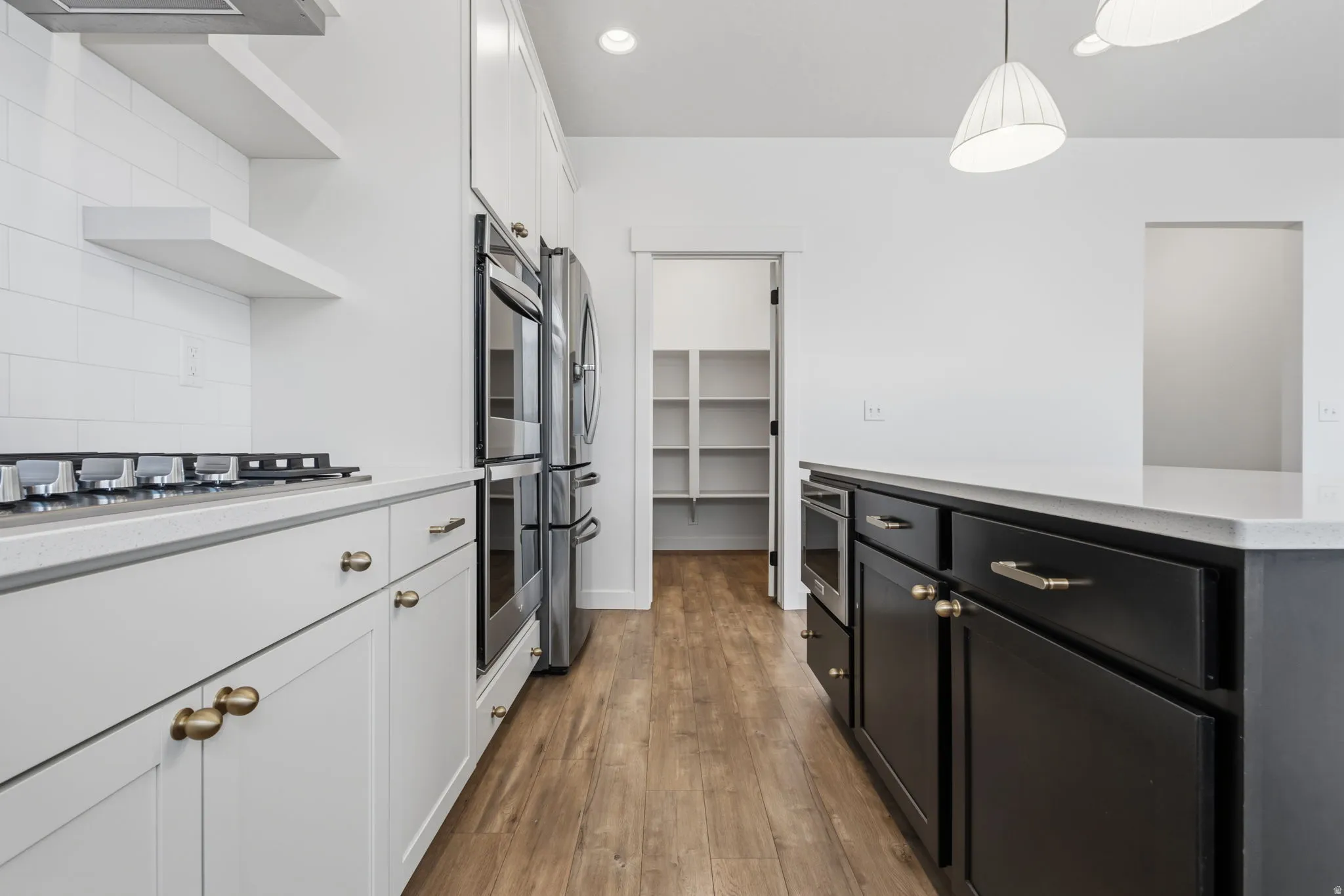 Modern kitchen featuring wood-finish flooring, white subway tile backsplash, and white cabinetry with brass hardware