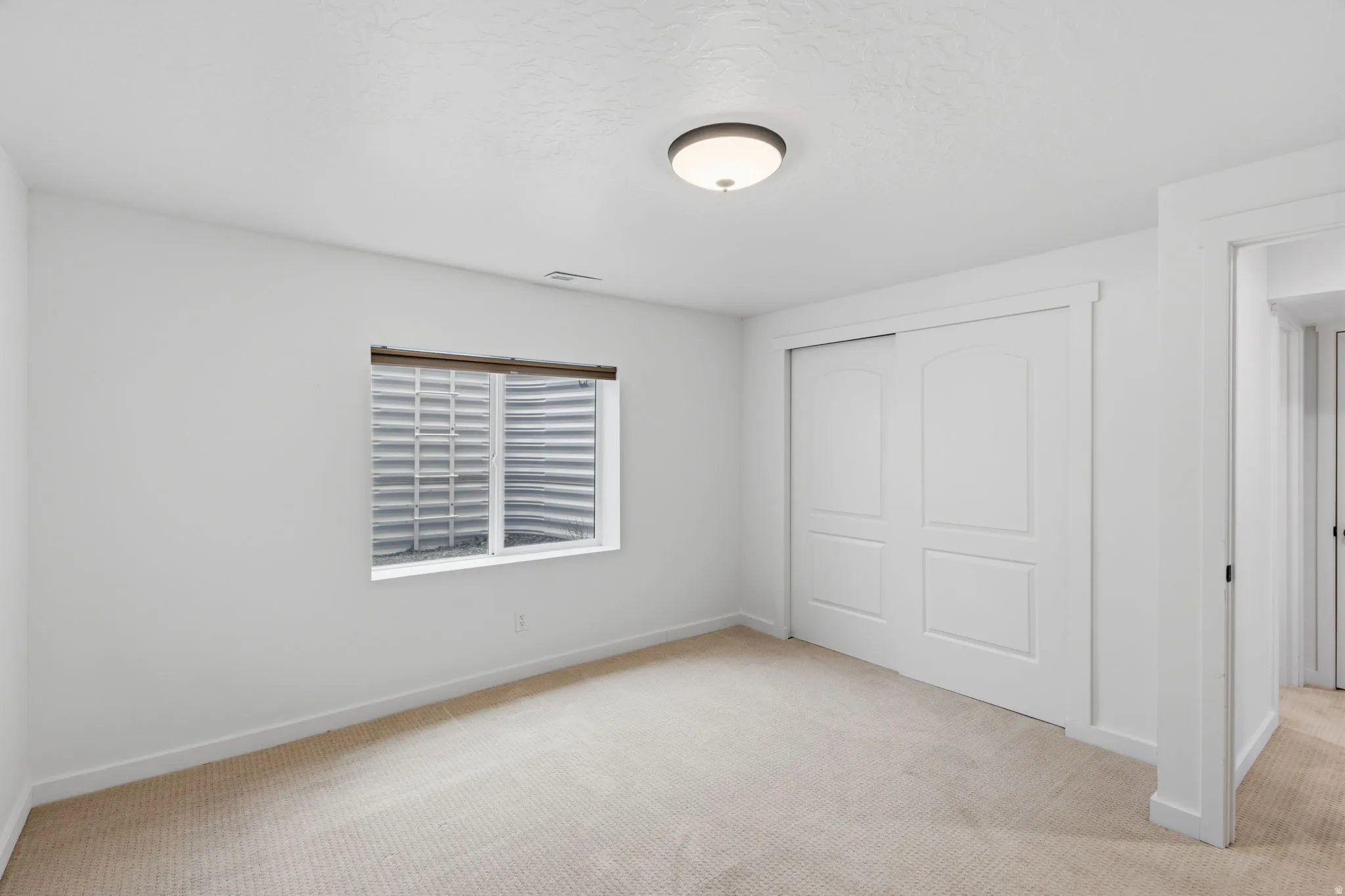 Carpeted room featuring a window with blinds, a flush mount ceiling light, and white sliding closet doors with arched panel details