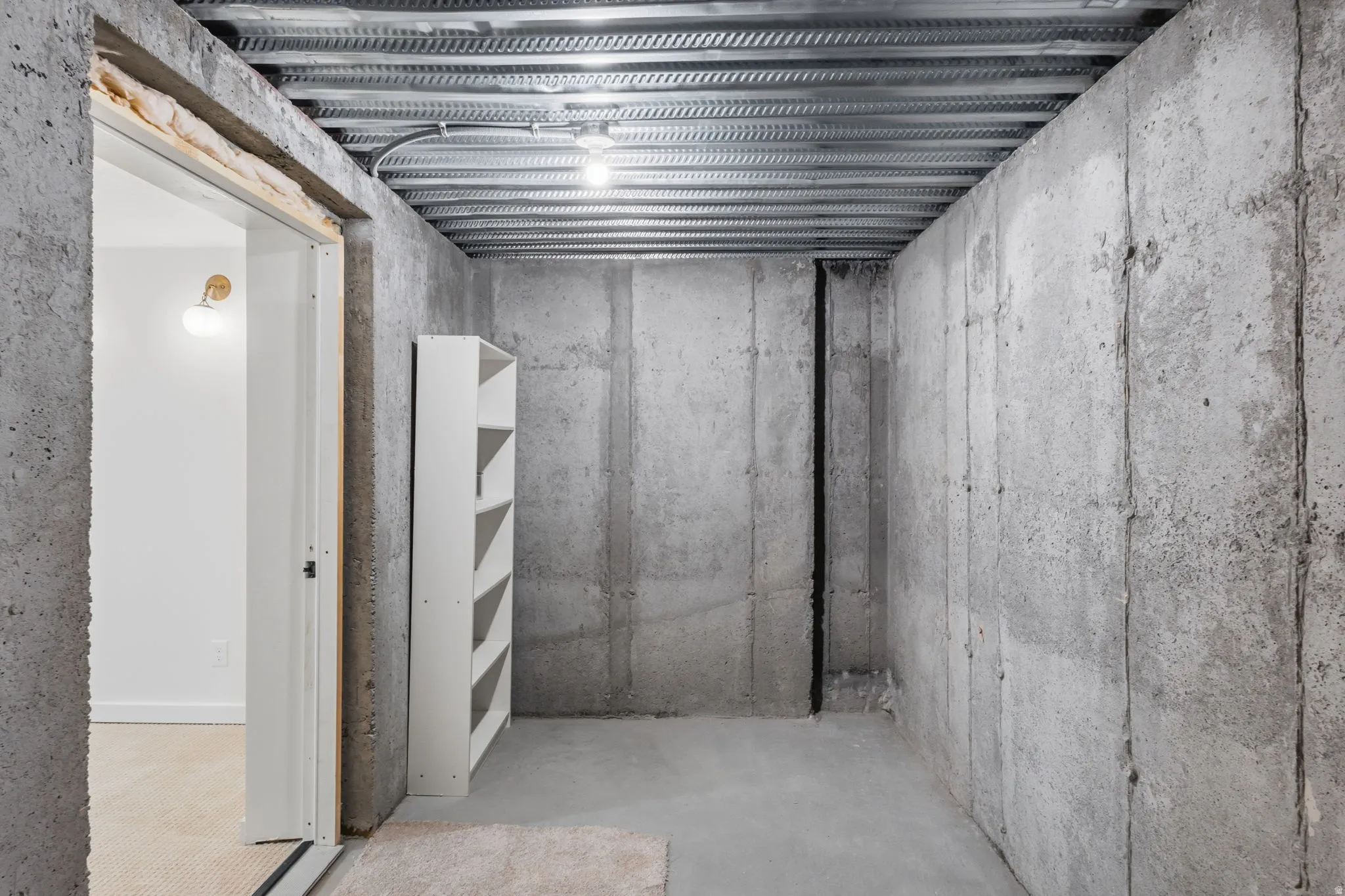 Unfinished concrete basement space featuring bare concrete walls and exposed ceiling joists