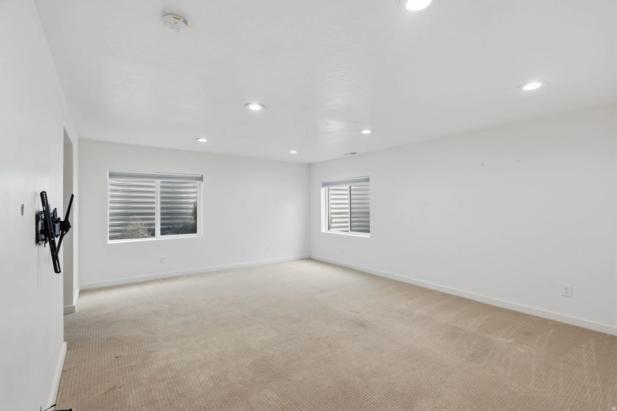 Spacious interior room featuring light-toned carpet, recessed ceiling lighting, and multiple windows with horizontal blinds