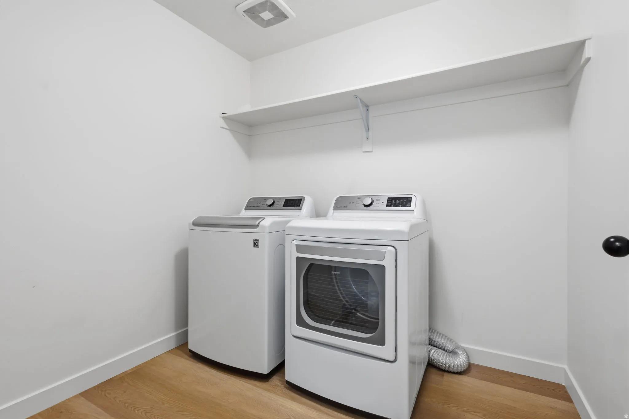 Dedicated laundry space featuring wood-finish flooring and a white wall shelf