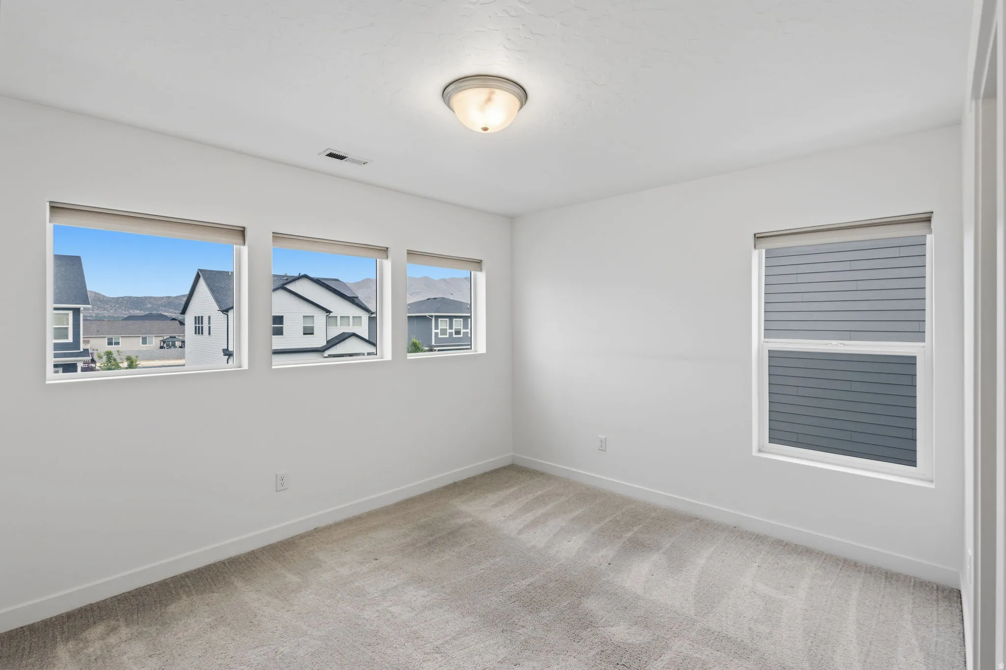 Carpeted room featuring multiple windows with roller shades, white walls, and a flush mount ceiling light