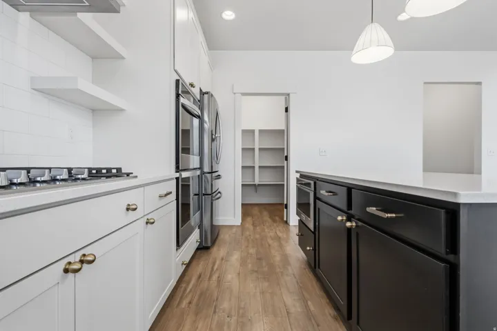 Modern kitchen featuring wood-finish flooring, white subway tile backsplash, and white cabinetry with brass hardware