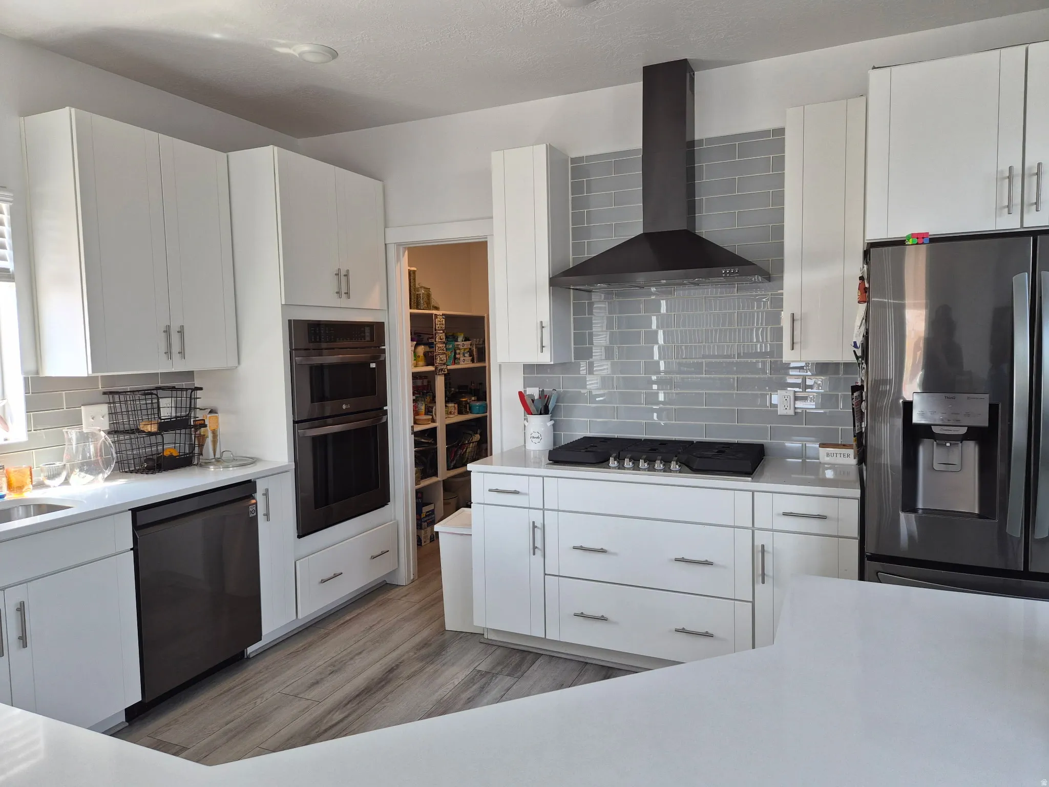 Contemporary kitchen featuring white cabinetry, light gray subway tile backsplash, stainless steel appliances, a built-in double oven, and a walk-in pantry