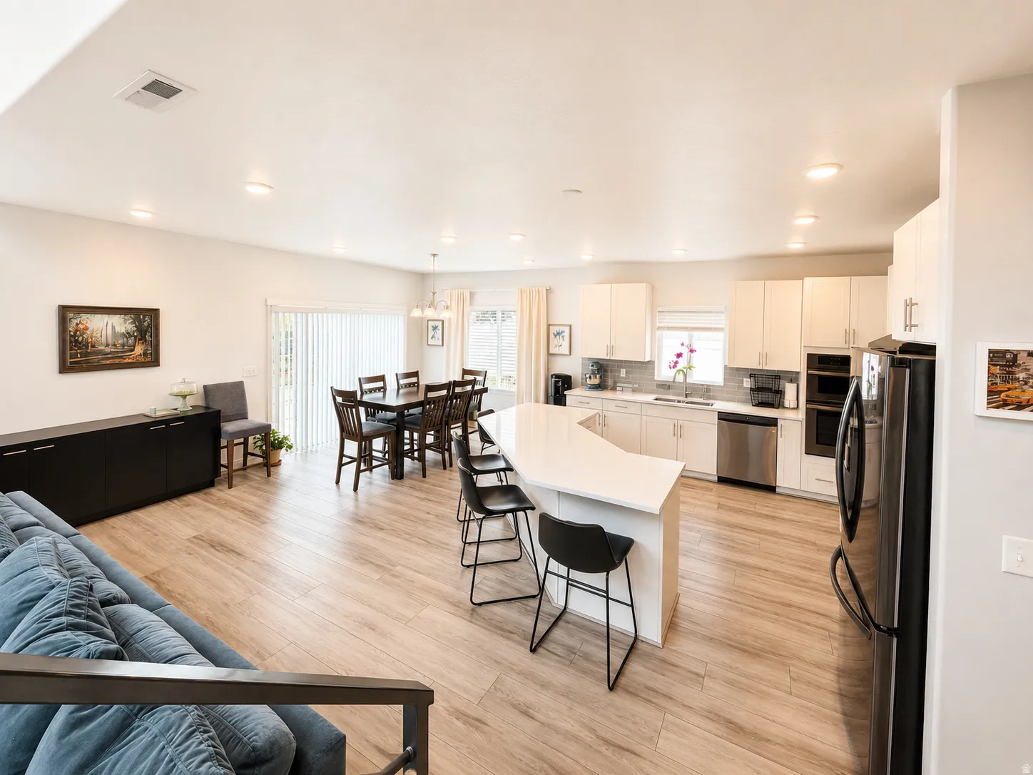 Open-concept living area featuring wood-finish flooring, recessed lighting, and a kitchen with white cabinetry and stainless steel appliances