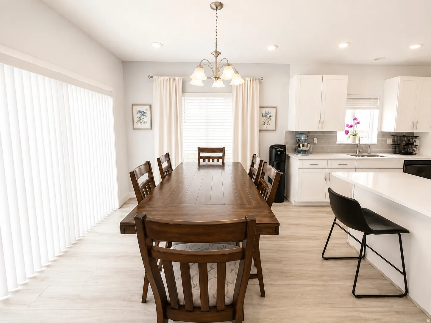 Open-concept dining and kitchen space featuring light wood-finish flooring, white cabinetry with silver hardware, a neutral tile backsplash, and an island with counter seating