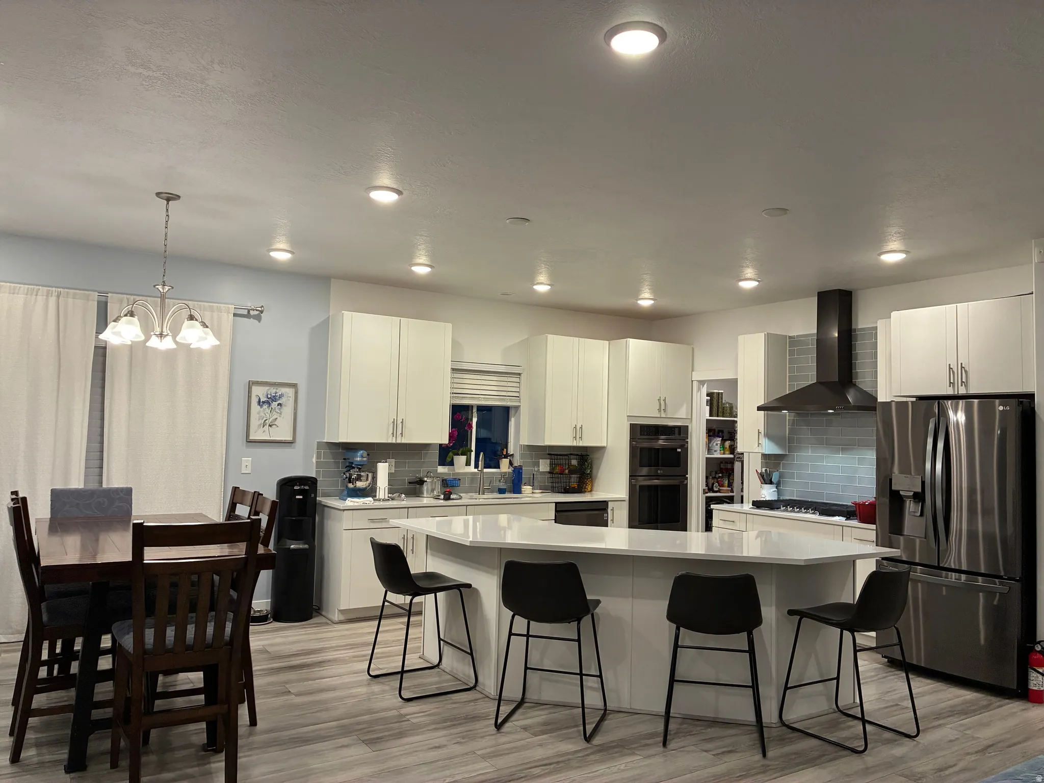 Kitchen featuring a large island with seating, white cabinetry, integrated double ovens, and a black range hood