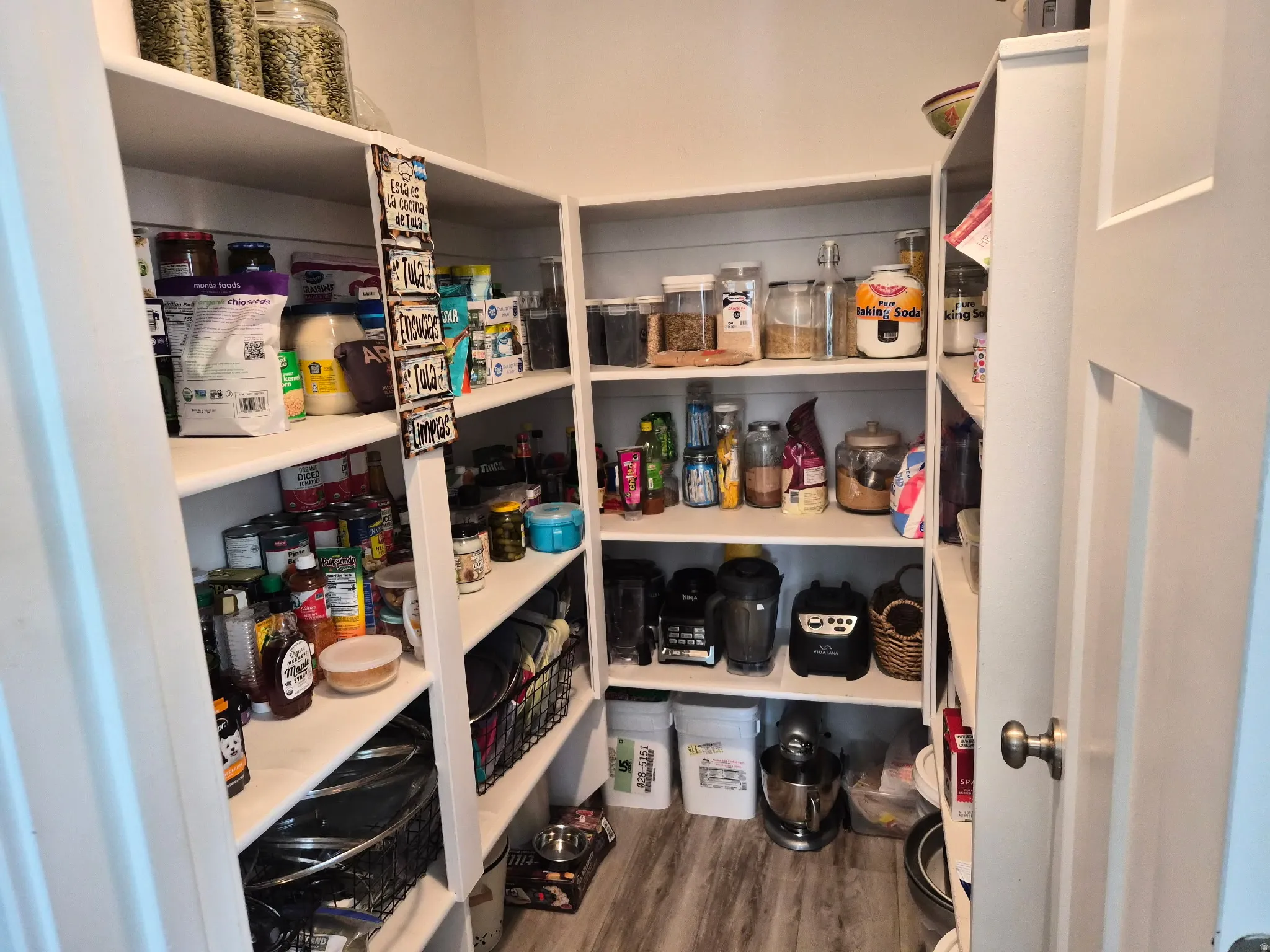 Walk-in pantry featuring extensive built-in shelving, light wood-finish flooring, and a white paneled door with a brushed nickel knob