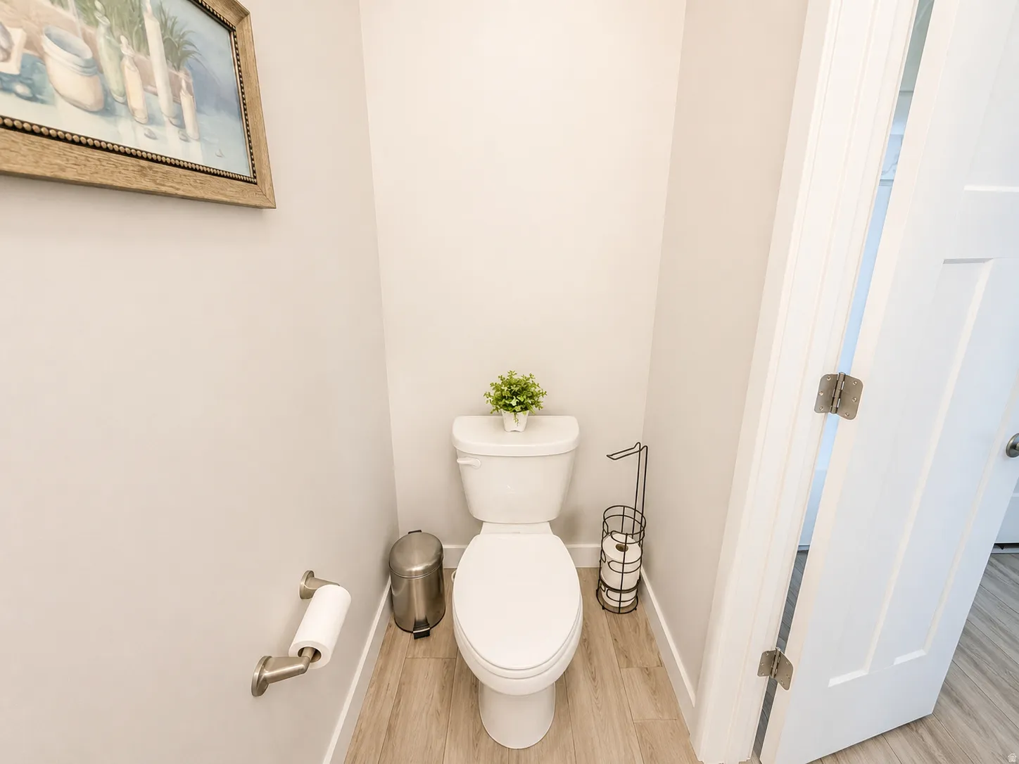 White toilet with a dual-flush mechanism, wood-finish flooring, and light-colored walls