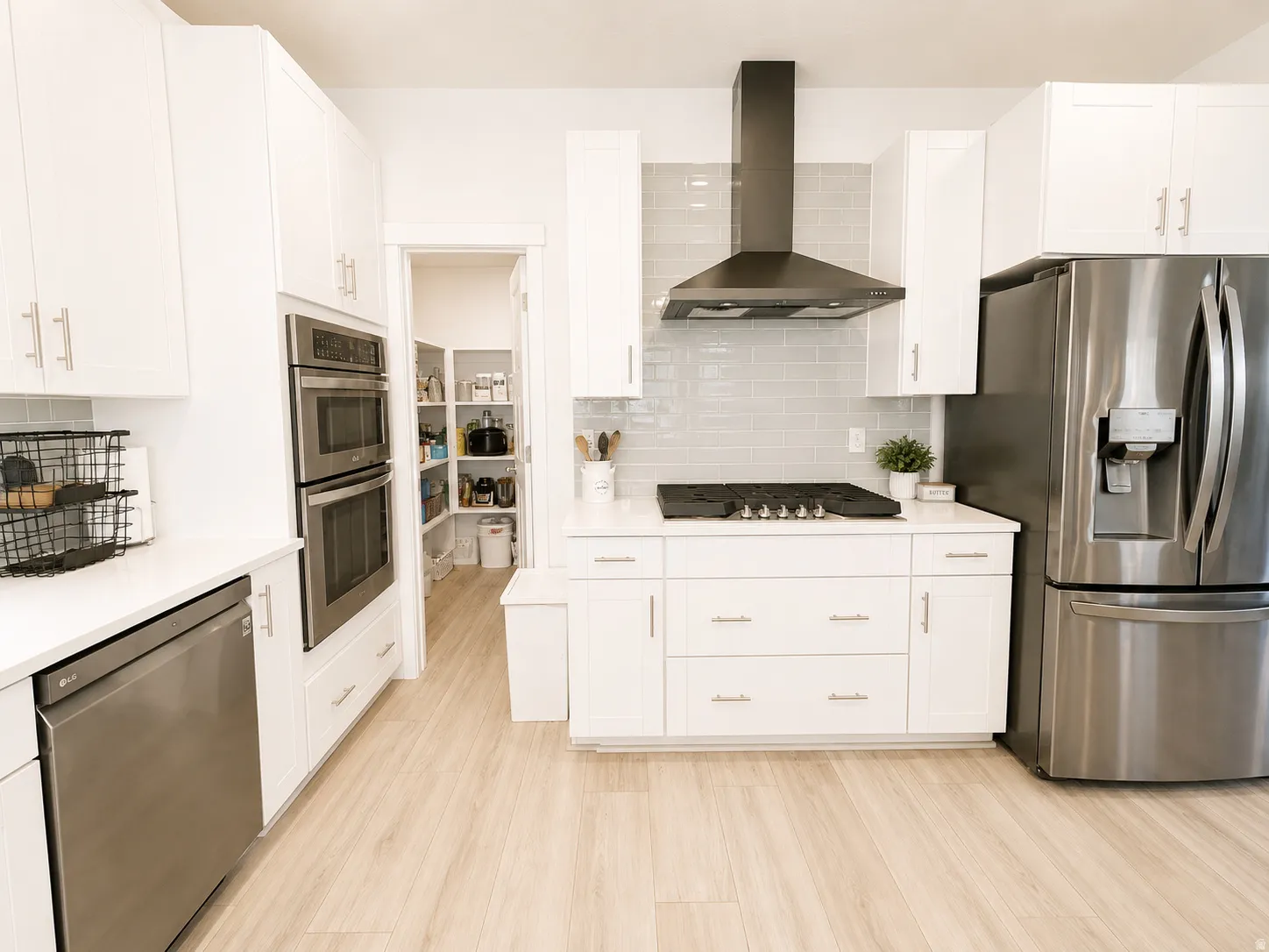 Sleek kitchen featuring white cabinetry, light wood-finish flooring, stainless steel appliances, and a gray subway tile backsplash