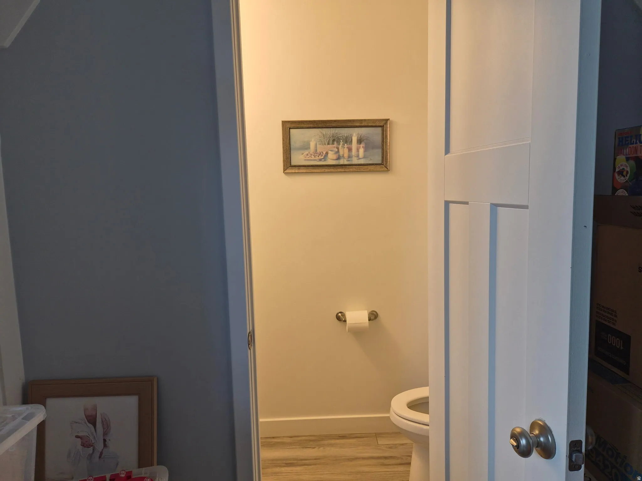 Private water closet featuring light-toned walls and wood-finish flooring