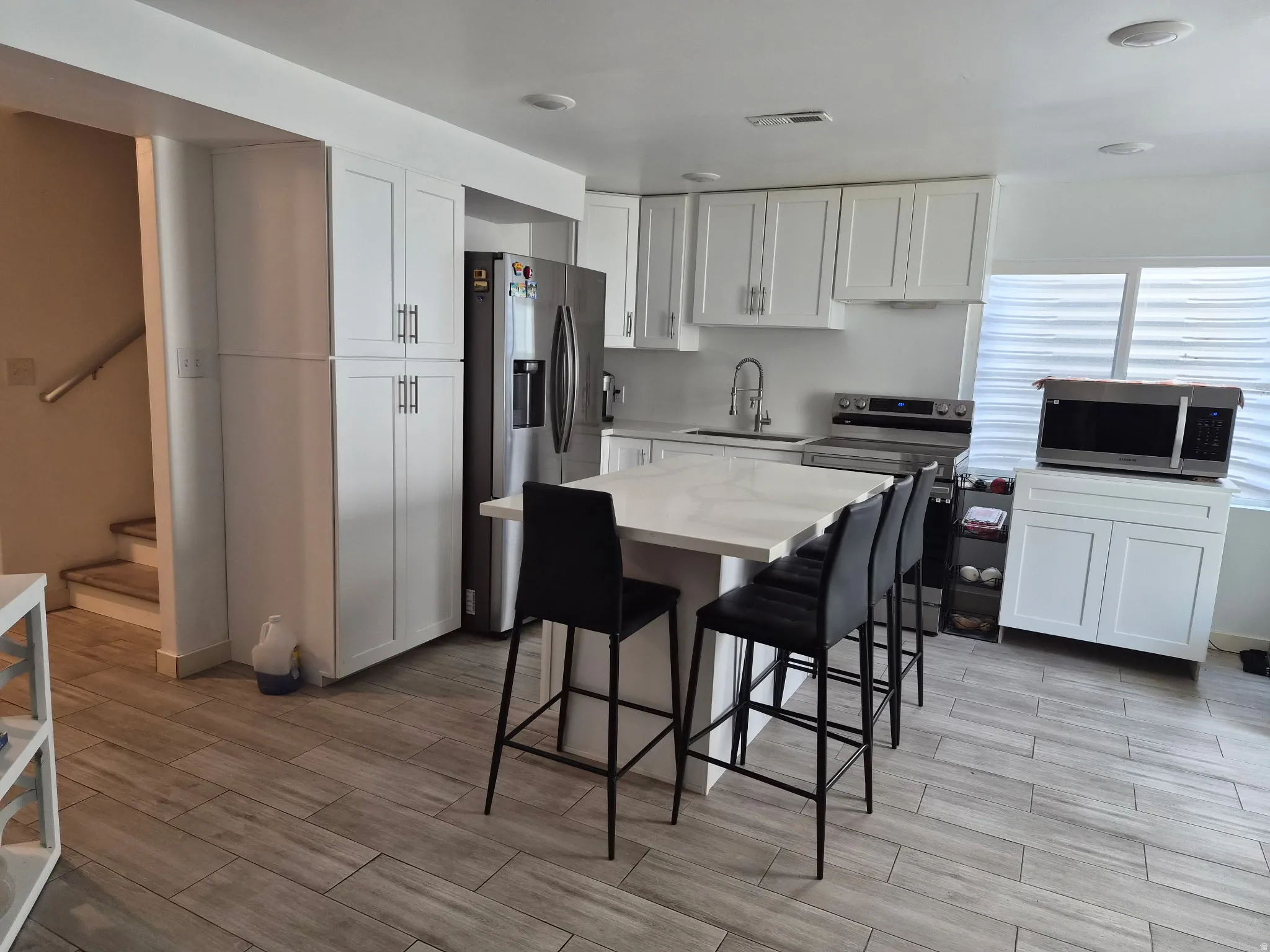 Modern kitchen featuring white shaker cabinetry, stainless steel appliances, a center island with a stone-finish countertop, and wood-finish flooring