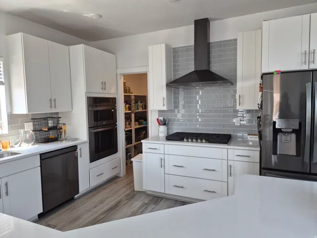Contemporary kitchen featuring white cabinetry, light gray subway tile backsplash, stainless steel appliances, a built-in double oven, and a walk-in pantry