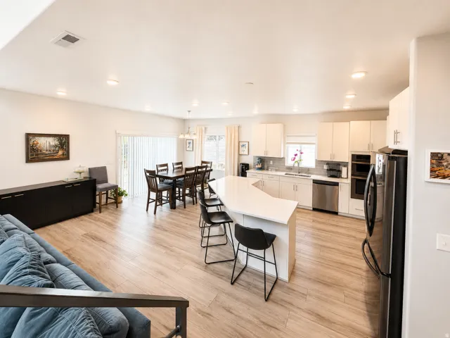 Open-concept living area featuring wood-finish flooring, recessed lighting, and a kitchen with white cabinetry and stainless steel appliances