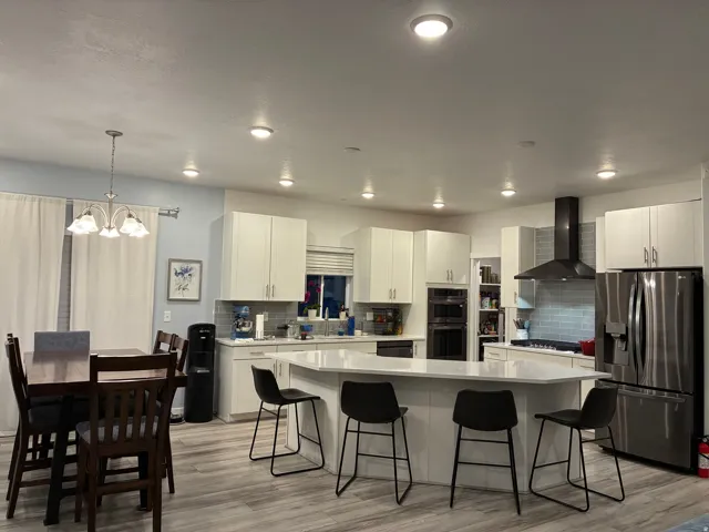 Kitchen featuring a large island with seating, white cabinetry, integrated double ovens, and a black range hood