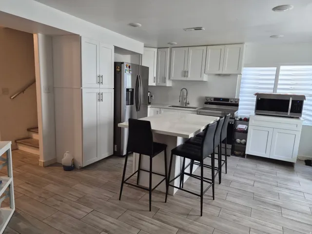 Modern kitchen featuring white shaker cabinetry, stainless steel appliances, a center island with a stone-finish countertop, and wood-finish flooring