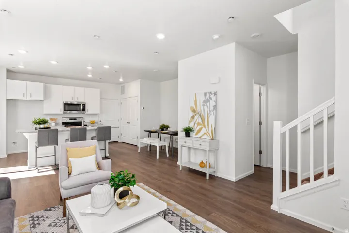 Open-concept living space featuring wood-finish flooring, recessed lighting, and a white kitchen with stainless steel appliances