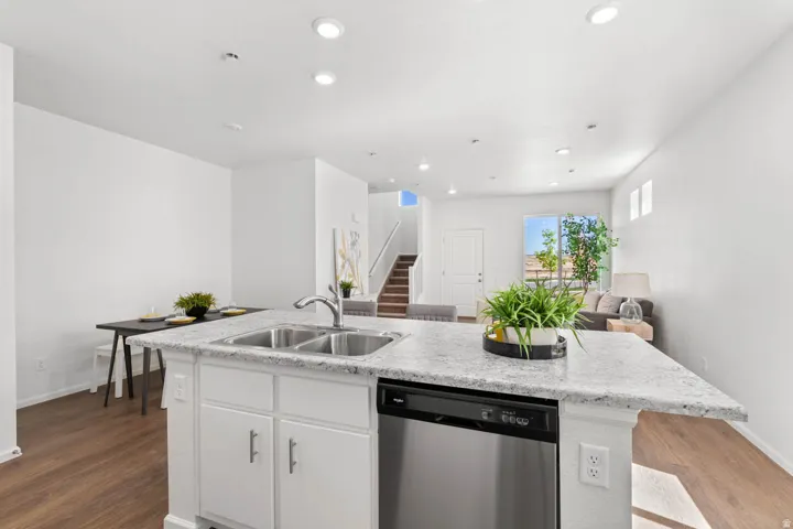 Kitchen island featuring a double basin stainless steel sink, stainless steel dishwasher, white cabinetry with silver hardware, and a light-toned speckled countertop