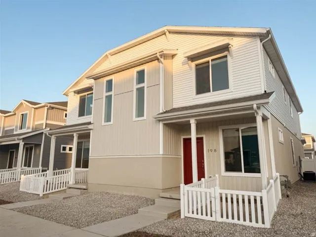 Contemporary townhouse exterior featuring a warm neutral palette, a striking red entry door, white vinyl fencing, and gravel landscaping