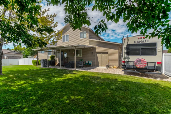 Spacious backyard featuring a covered patio, expansive lawn, gravel parking area, two-story exterior siding, and a dedicated storage shed