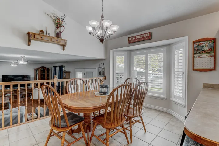 Dining area featuring a bay window with plantation shutters, tile flooring, and a decorative chandelier