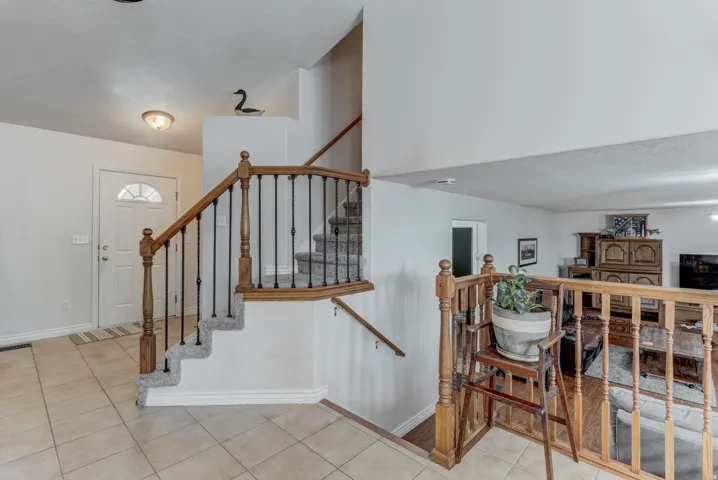 Entryway featuring tile flooring, a white paneled door with an arched window, and a carpeted staircase with wood handrails and black metal spindles