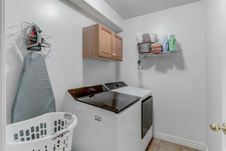 Dedicated laundry area featuring white appliances, a light wood-finish wall cabinet, and a wall-mounted shelving unit
