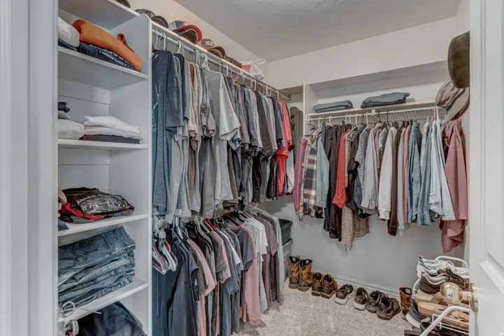 Walk-in closet featuring white shelving units, multiple hanging rods, built-in upper shelving, and neutral carpeting