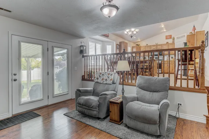 Wood-finish flooring throughout, featuring french doors with exterior access, a decorative hanging light fixture, and a partial baluster-style railing