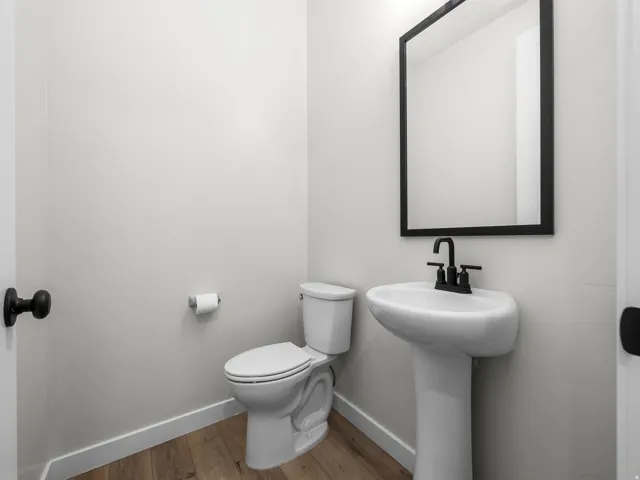 Pedestal sink with matte black faucet, framed mirror, and wood-finish flooring