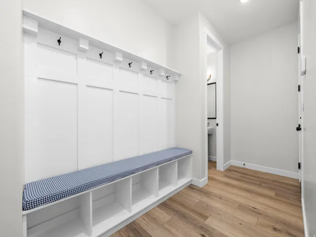 Mudroom featuring built-in bench seating with cubby storage, integrated wall hooks, light wood-finish flooring, and recessed lighting