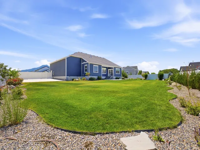 Expansive backyard featuring a manicured lawn, gravel landscaping, established perimeter shrubbery, and a full vinyl privacy fence