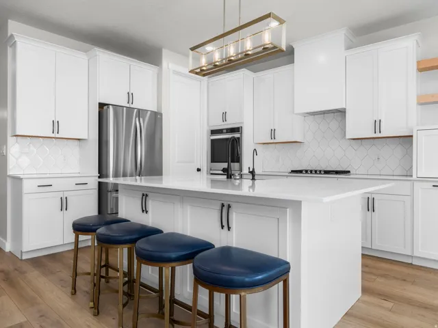 Modern kitchen featuring an expansive center island with seating, white shaker cabinetry, stainless steel appliances, and wood-finish flooring