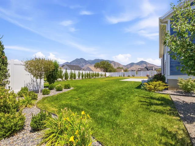 Expansive backyard featuring a manicured lawn, established landscaping, and a white privacy fence