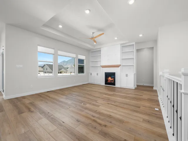Spacious interior featuring wood-finish flooring, a tray ceiling with recessed lighting, and a built-in entertainment center with shelving and a fireplace