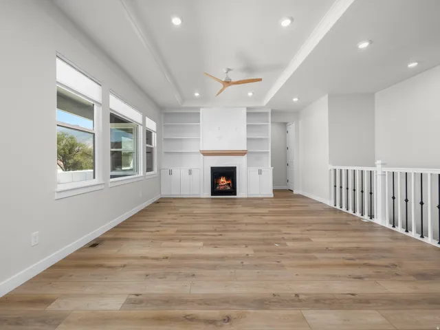 Living space featuring wood-finish flooring, a contemporary fireplace with a wood mantel, built-in shelving, a modern ceiling fan, and recessed lighting