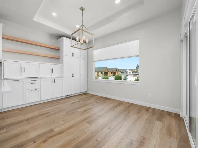 Bright open-concept space featuring extensive white cabinetry, wood-finish flooring, a contemporary chandelier, a large horizontal window, and a sliding glass door