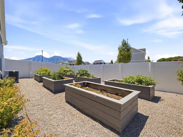 Gravel patio featuring multiple raised garden beds, a white privacy fence, and mature landscaping