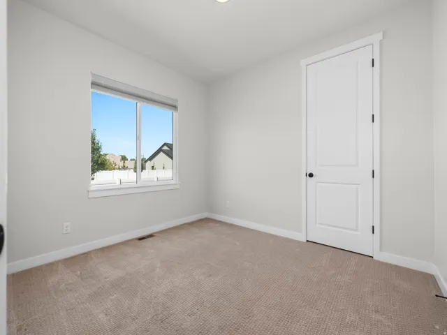 Neutral-toned room featuring a large window with white trim, light-colored carpet flooring, and a white paneled door with a matte black handle