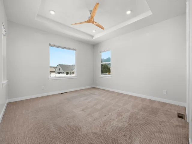 Spacious interior featuring a tray ceiling with recessed lighting, a contemporary ceiling fan, and two large windows