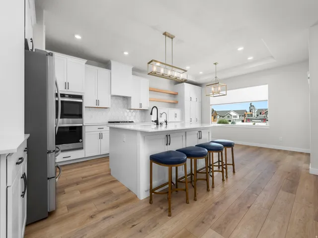 Gourmet kitchen featuring a large central island with seating, white shaker cabinetry, stainless steel appliances, and wood-finish flooring