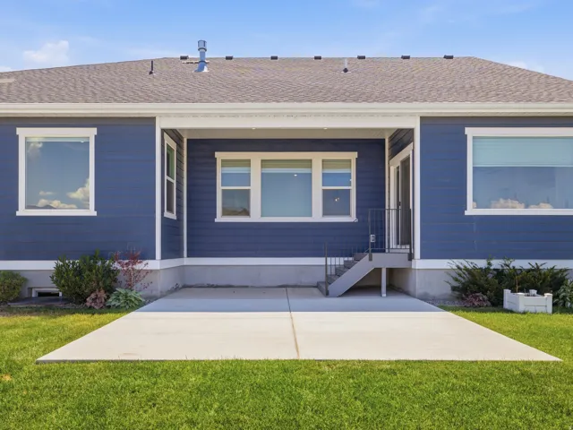 Rear exterior featuring a concrete patio, blue siding, white window trim, and a shingle roof