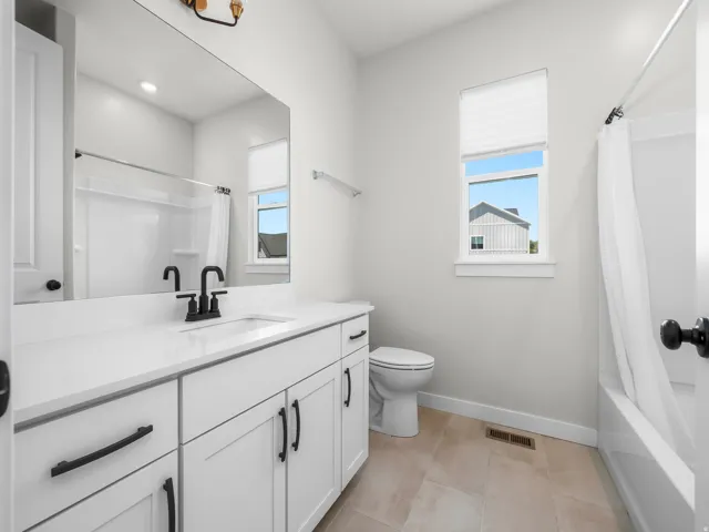 Bathroom featuring a white vanity with extensive counter space, matte black fixtures, a rectangular mirror, a bathtub with an integrated shower, and light-toned tile flooring