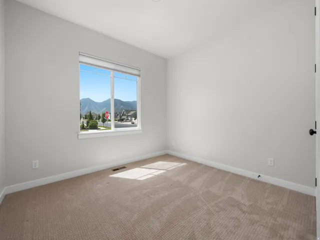 Bright interior space featuring neutral wall tones, carpet flooring, a large window, and mountain scenery