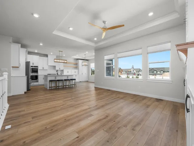 Expansive open-concept living space featuring wood-finish flooring, a tray ceiling with recessed lighting, and a modern ceiling fan