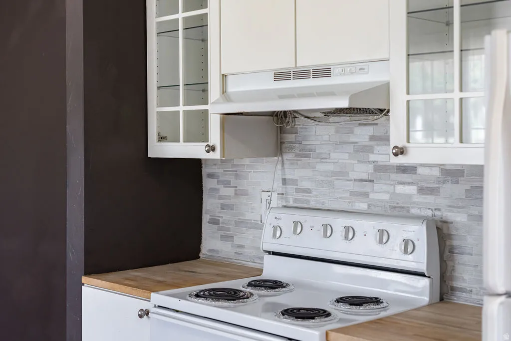 Kitchen featuring a white electric range, light wood-finish countertops, and a gray-toned subway tile backsplash