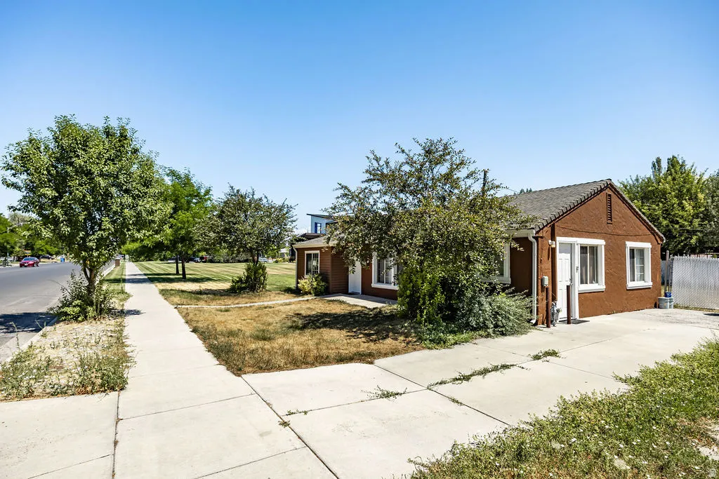 Brown exterior with white trim, featuring a side driveway, concrete sidewalk, and mature landscaping