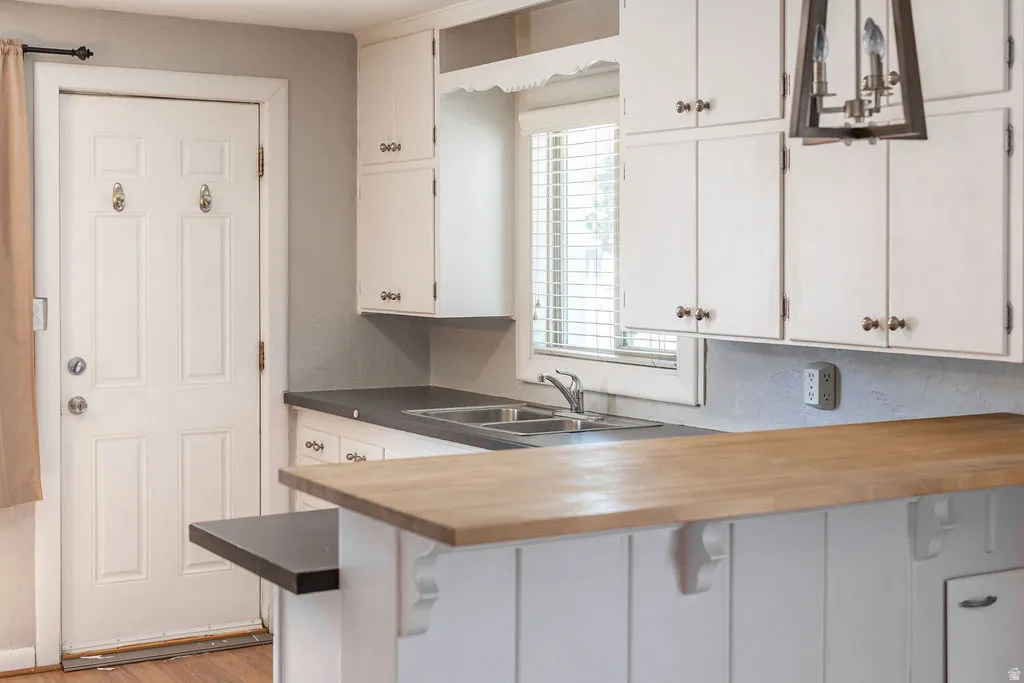 Kitchen featuring white cabinetry, dark countertops, a double basin sink, and a wood-finish breakfast bar with decorative corbels