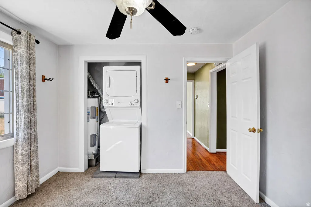 Room featuring a stacked white washer and dryer unit, carpet flooring, a window, and a ceiling fan